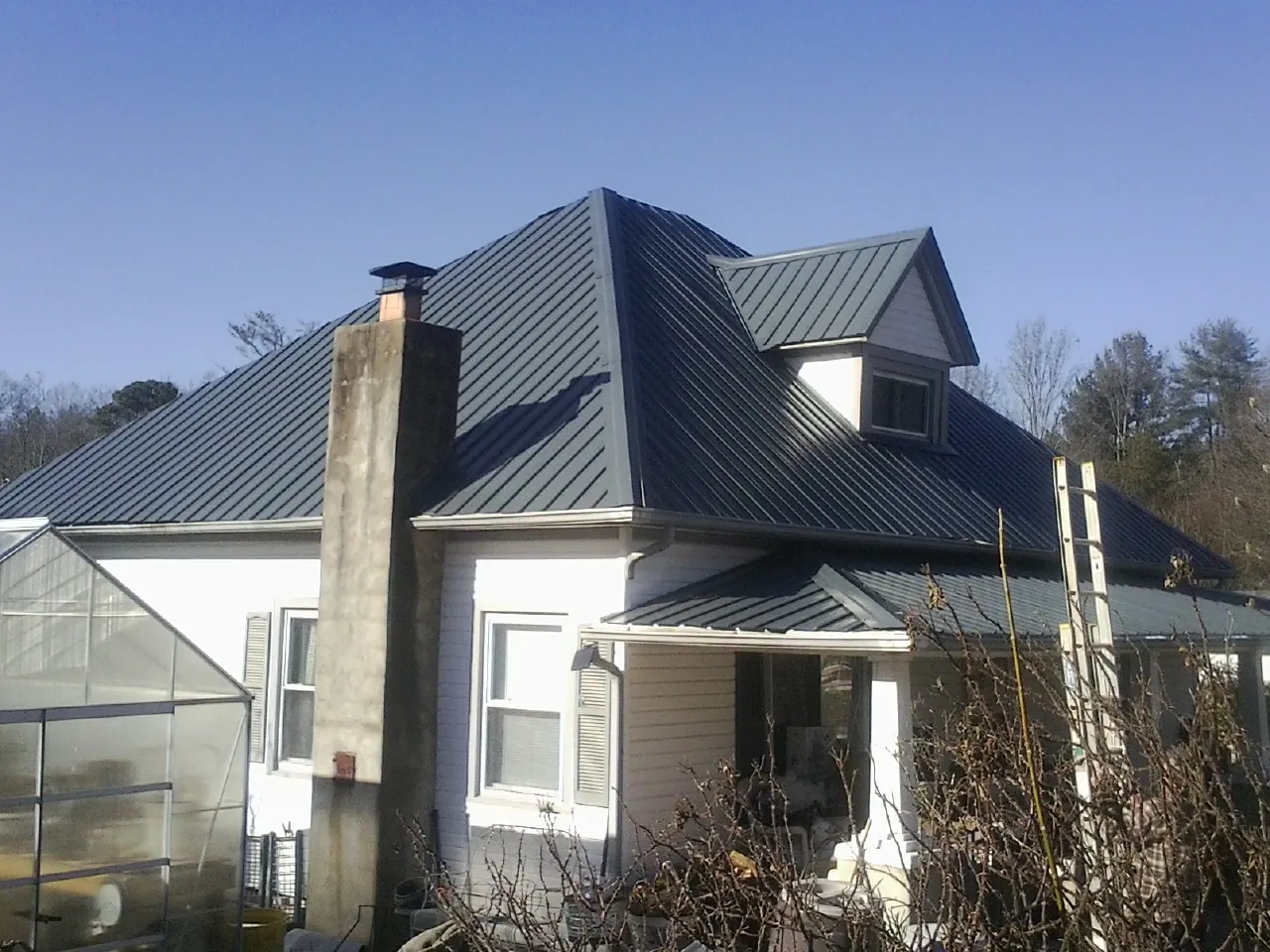 Dark blue standing seam metal roof on a white farmhouse with dormer — Slate & Tile Roof Repair by Roofing Brothers in Rockingham