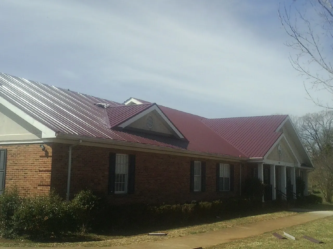 Red metal roof with gabled entries on a long brick building, from a Hail Damage Roof Repair job in Rockingham