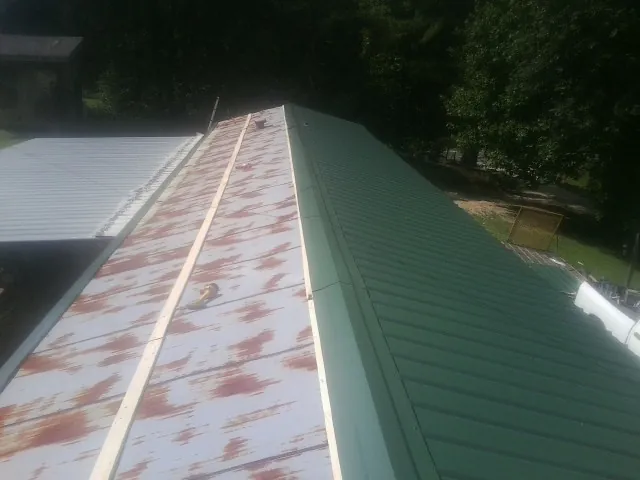 Old rusted panels beside newly installed green metal roofing — Wind Damage Roof Repair by Roofing Brothers in Rockingham