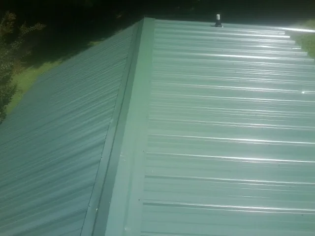 New green metal panels meeting at the ridge of a roof — Flat Roof Repair work by our crew in Rockingham