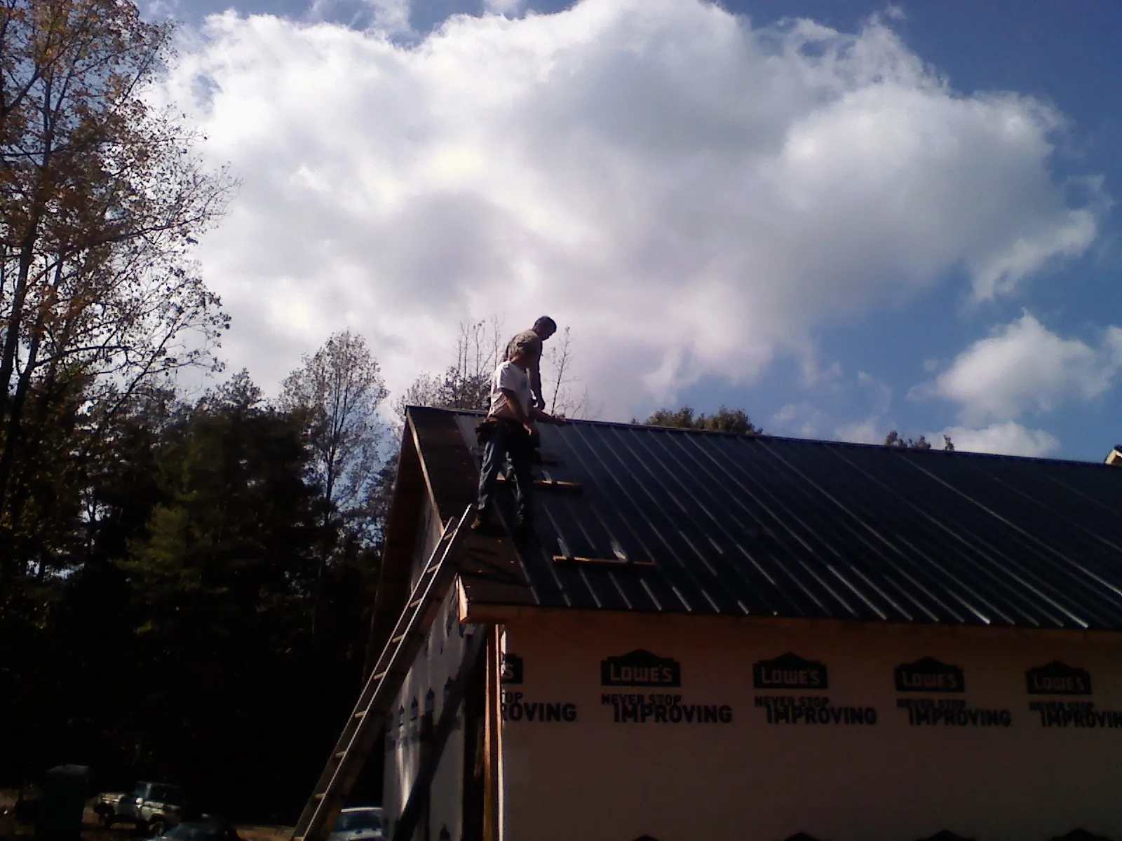 Roofer fastening dark metal panels high against a cloudy sky, from a Roof Inspection job in Rockingham