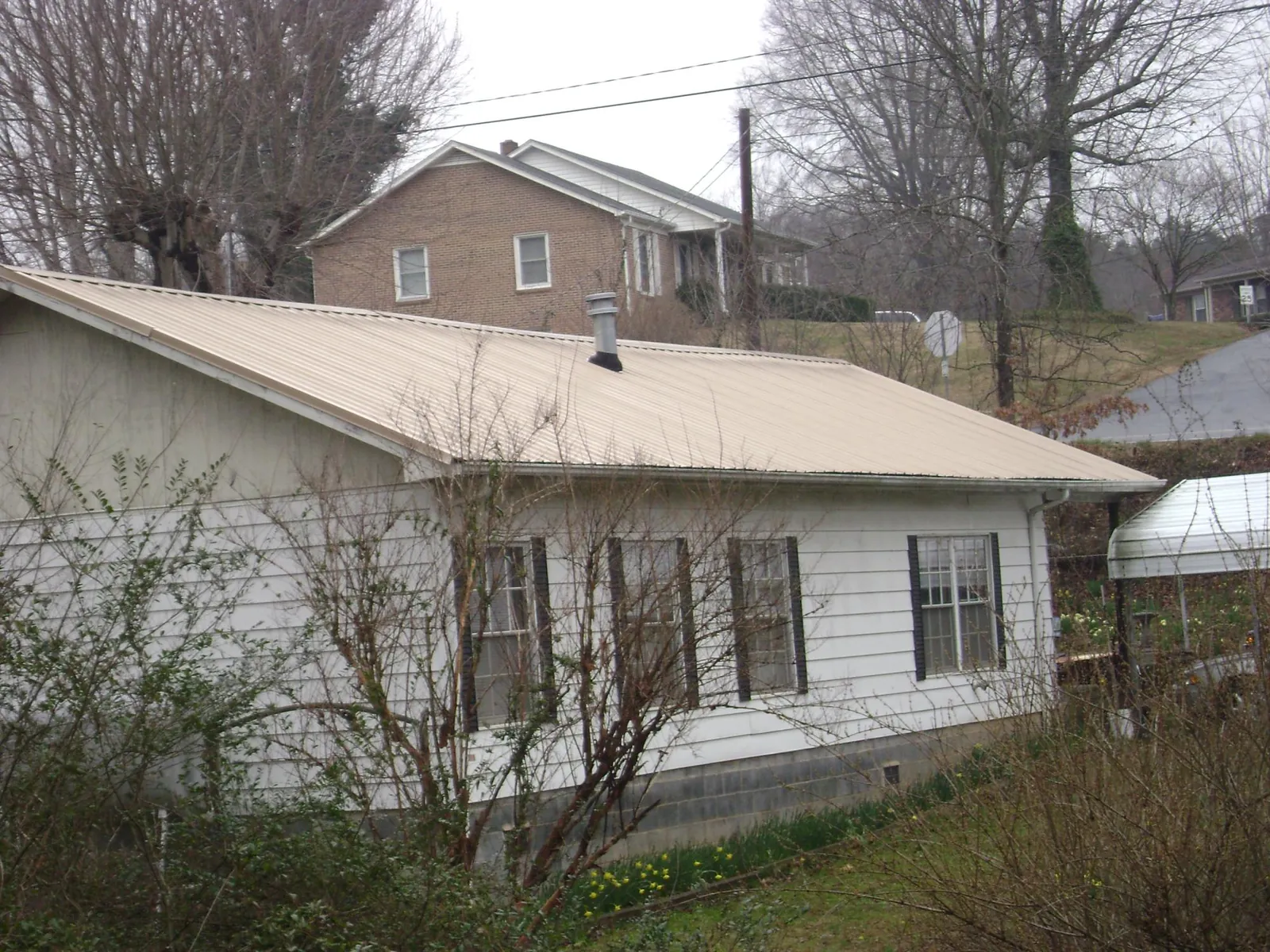 Tan metal roof on a white sided house set into a hillside — Commercial Roofing by Roofing Brothers in Rockingham