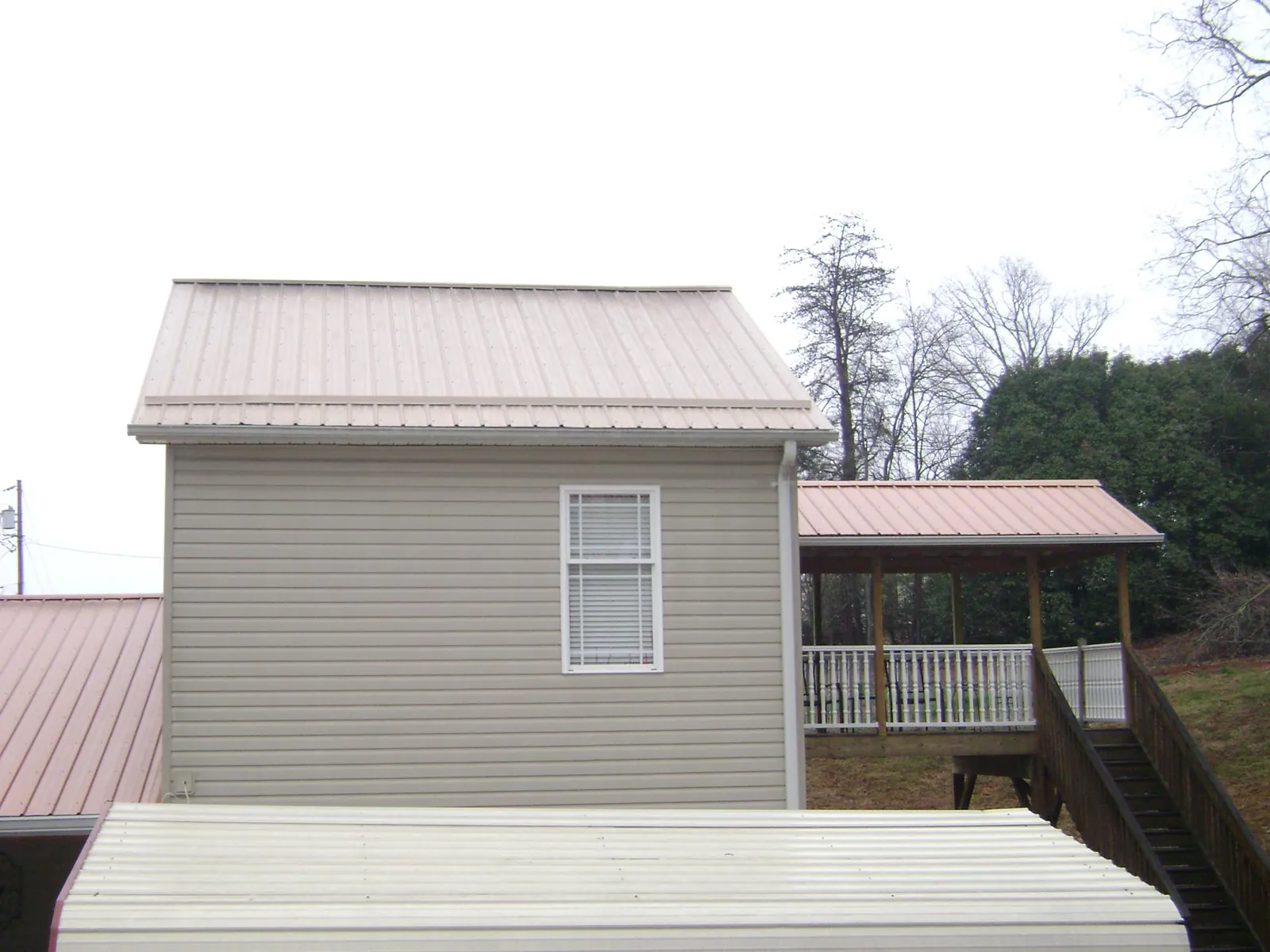Tan metal roofs on a two story addition and attached porch, from a Roof Replacement job in Rockingham