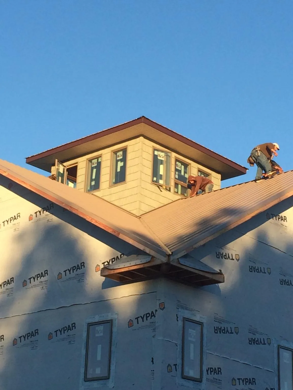 Roofers working around a rooftop cupola on a new metal roof at sunset — Roof Waterproofing in Rockingham by Roofing Brothers